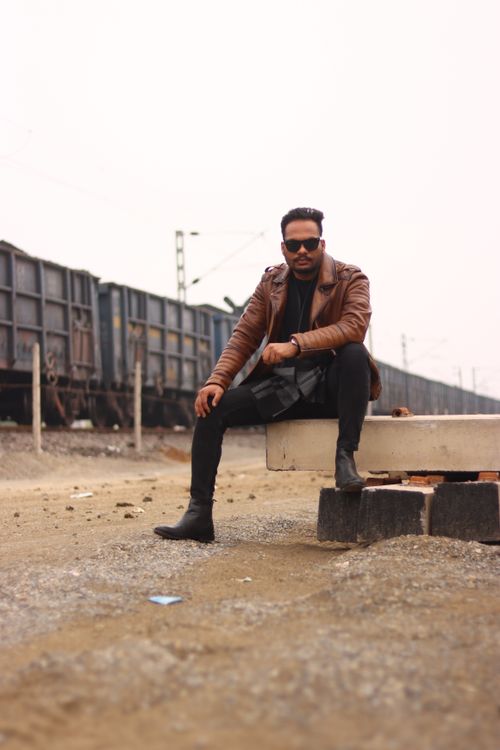 Free Man in a leather jacket posing beside railway wagons outdoors. Stock Photo