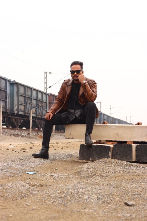Free Stylish man in leather jacket and sunglasses sitting outdoors near train tracks. Stock Photo