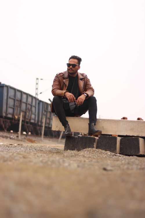 Free Fashionable man in leather jacket and sunglasses sitting near train tracks in a rural setting. Stock Photo