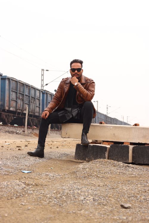 Free Cool fashion portrait of a man in a brown leather jacket sitting by railway tracks. Stock Photo