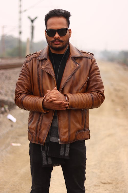 A man in a brown leather jacket standing on a train track