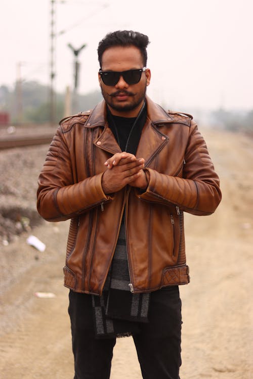 A man in a brown leather jacket standing on a train track