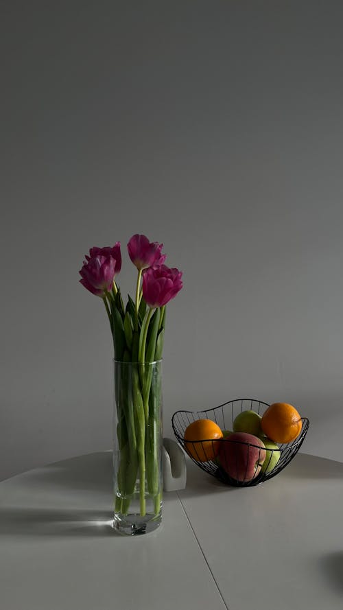 Vase with Purple Blooming Flowers and Fruits in a Bowl