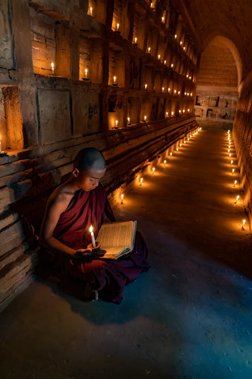 Child in Buddhist Monk Robes Sitting with Candles and Reading Book