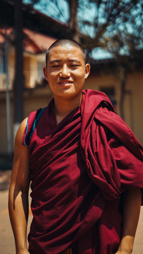Free A smiling young monk in a red robe during a sunny day outdoors. Ideal for cultural and lifestyle themes. Stock Photo