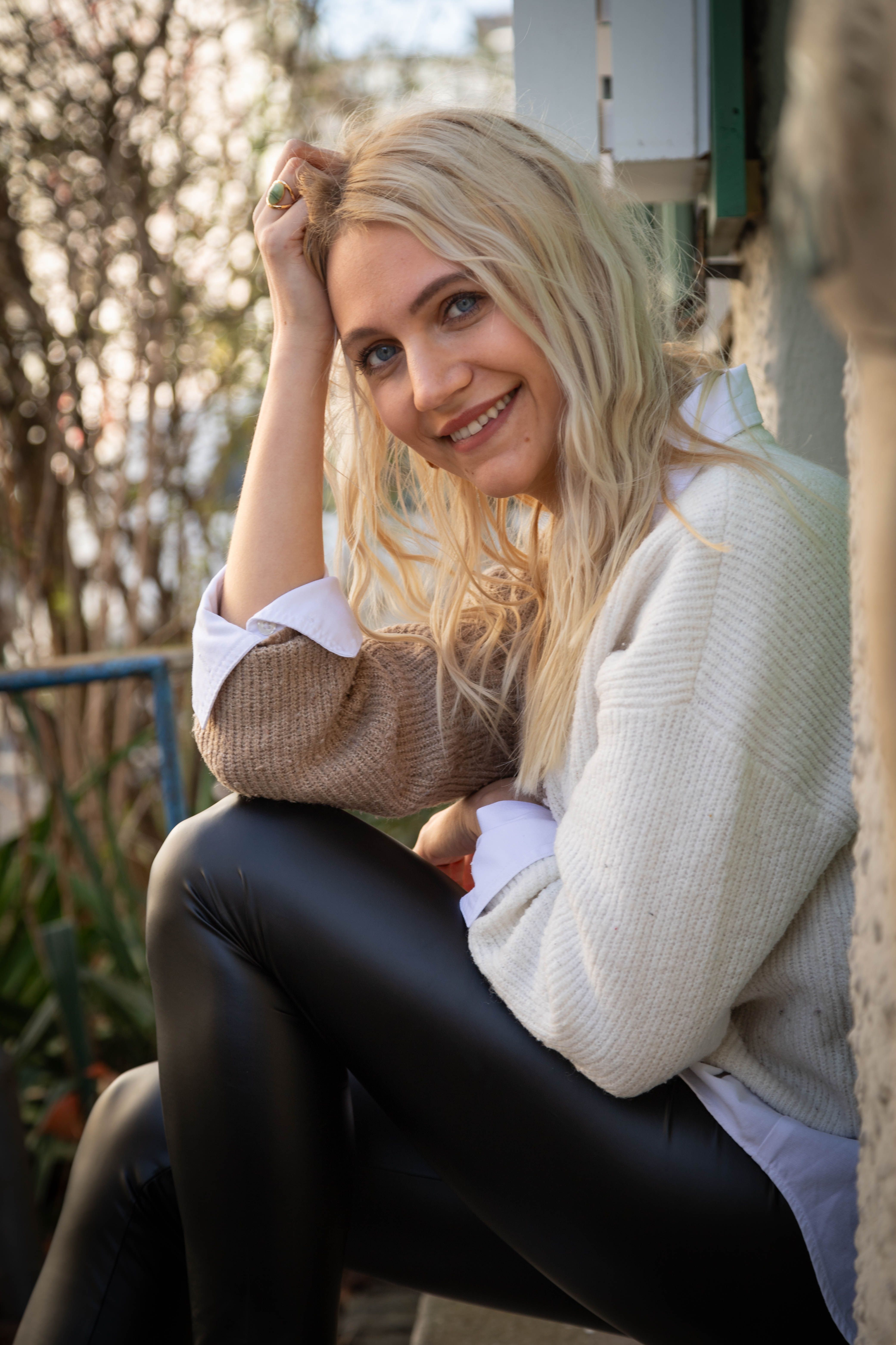 A smiling woman with blonde hair sitting casually outdoors in Munich.