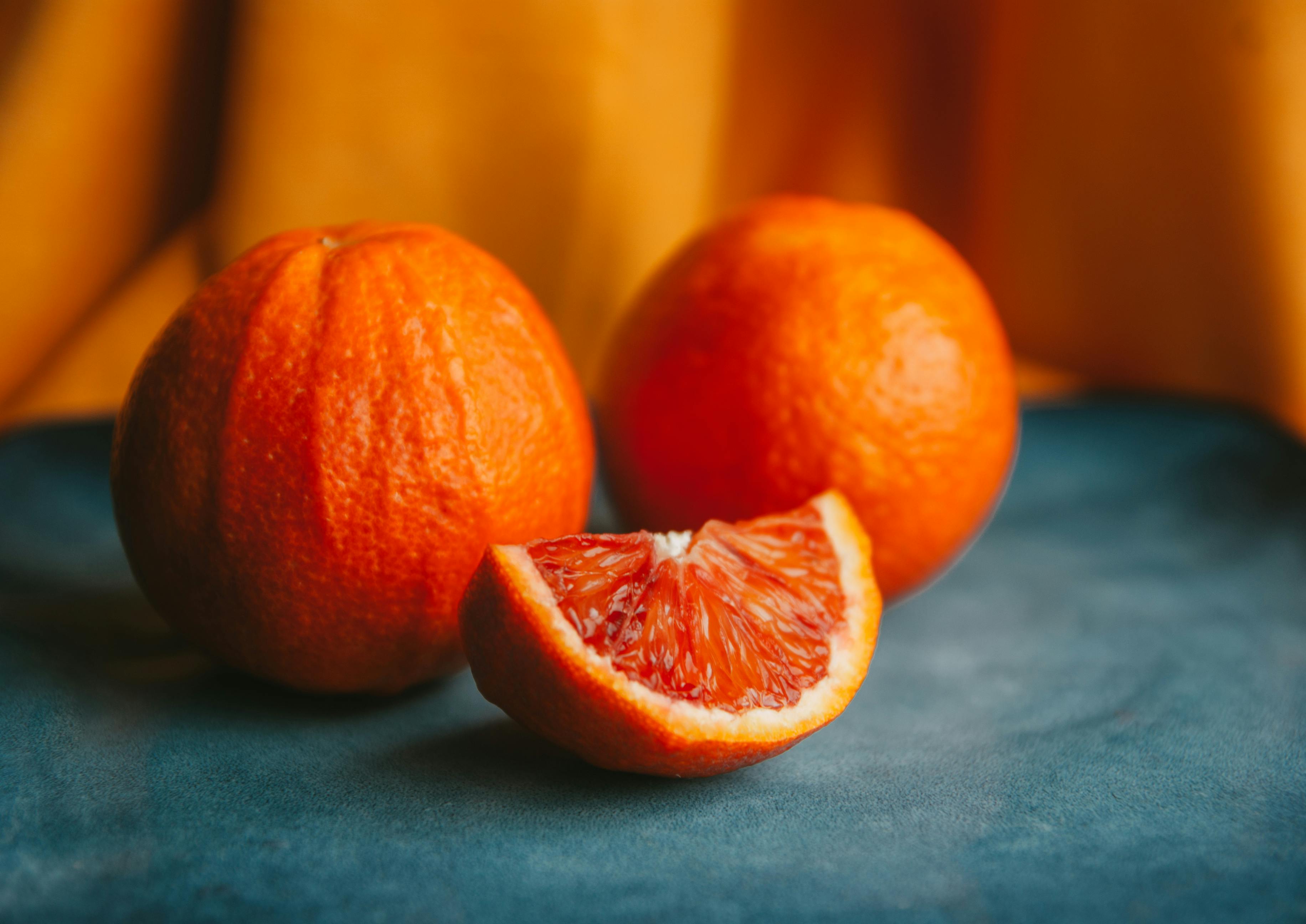 Close-up of fresh blood oranges with a slice on a vibrant blue and orange backdrop.