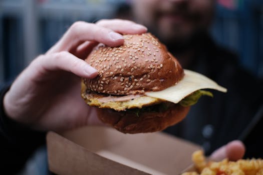 A person holding a cheeseburger with sesame seed bun, cheese, and lettuce in London, UK.