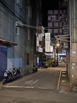 Explore a quiet Taiwanese alleyway at night, adorned with scooters and urban architecture.