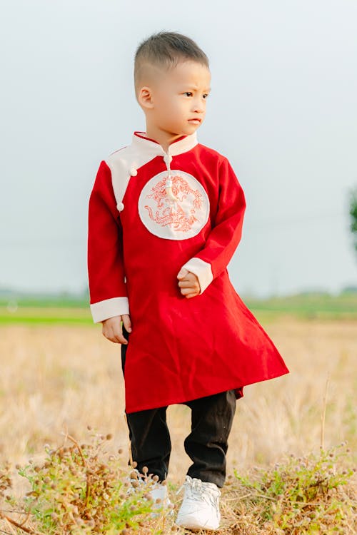A little boy in red and white clothing standing in a field
