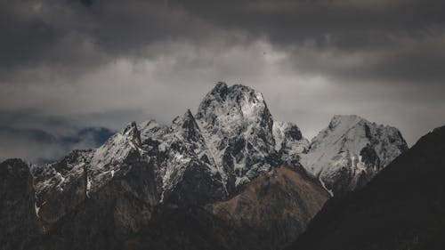 A mountain range with snow capped peaks under a cloudy sky
