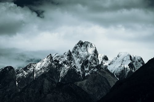 A mountain range with snow capped peaks under a cloudy sky