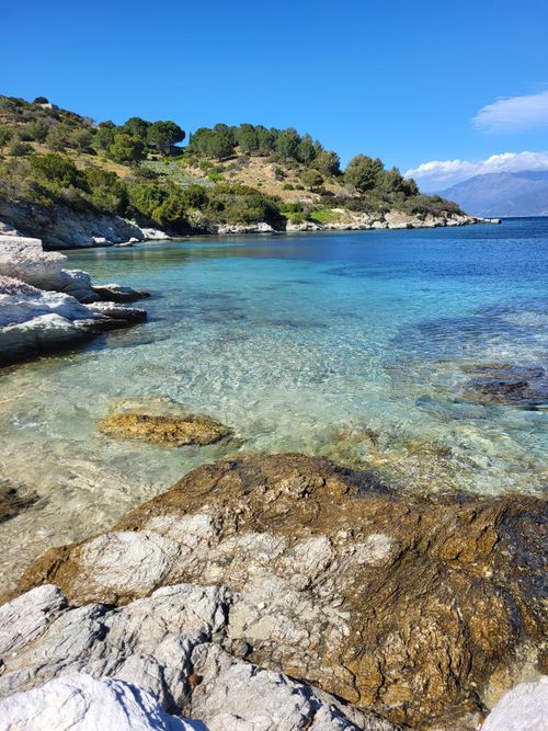 Free Beautiful coastal scene with clear blue waters and rocky shoreline under a bright blue sky. Stock Photo