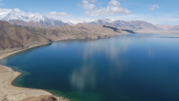 A breathtaking aerial view of a pristine lake surrounded by rugged mountains in Ngari Prefecture, Tibet.