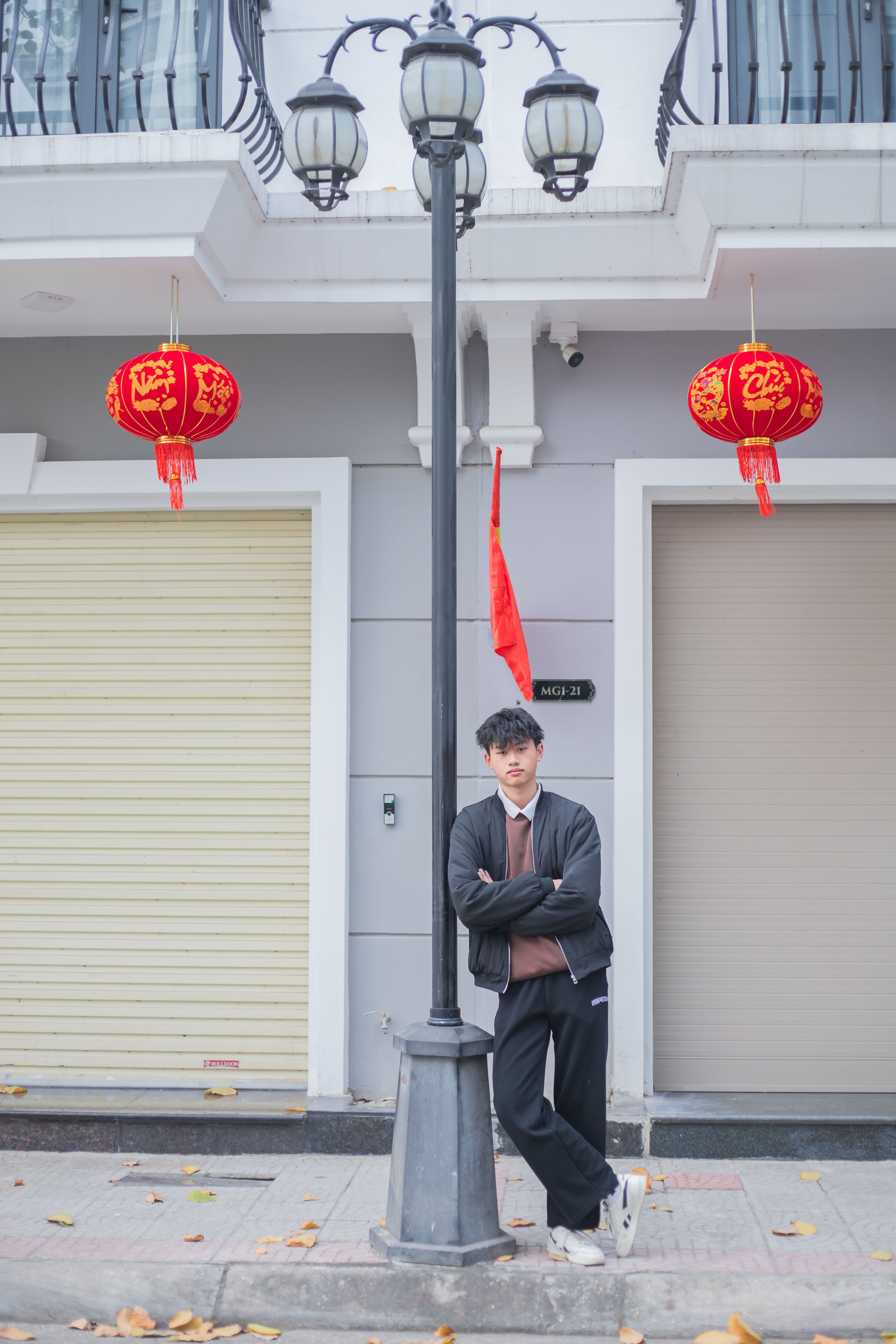 Young man posing by a street lamp with Chinese lanterns in an urban setting. Stylish and modern.