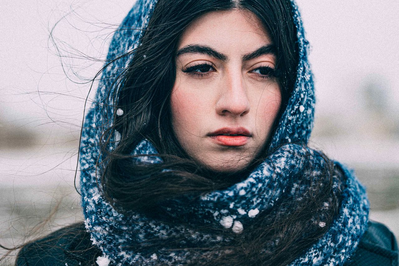 Close-up portrait of a woman in a blue knit scarf dusted with snow