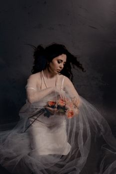 Artistic portrait of a woman in a white dress holding pink roses with a veil.