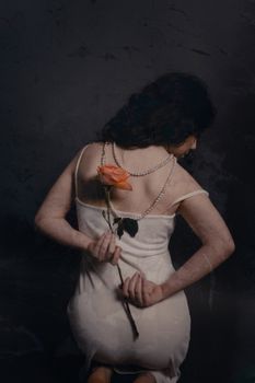 Back view of a woman in a white dress holding a rose, captured in a fashion studio setting.