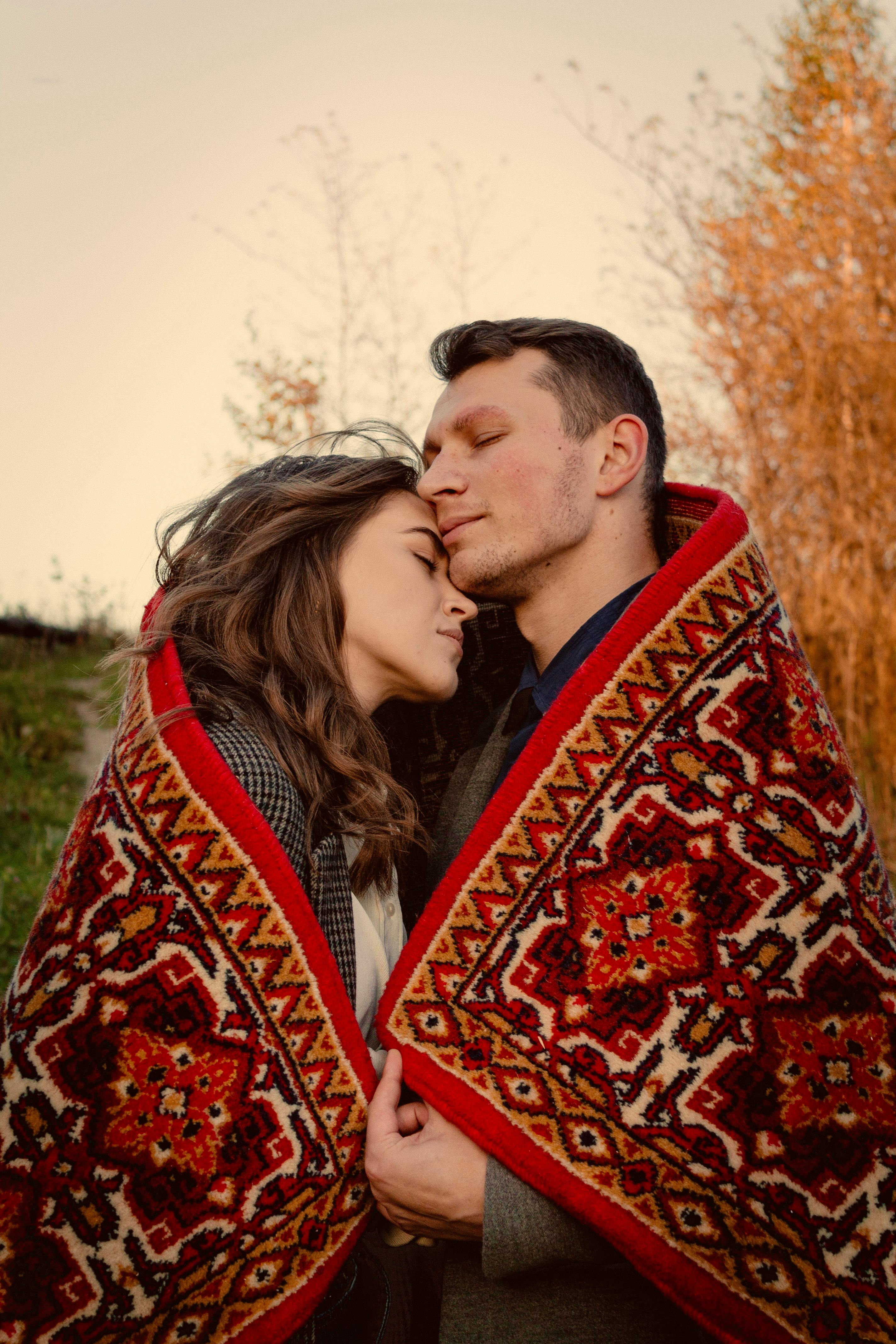A loving couple embraces outdoors, wrapped in a colorful blanket during fall in Lviv, Ukraine.