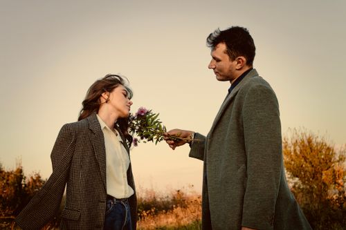 Free Couple in coats sharing a tender moment in the autumn countryside with flowers. Stock Photo