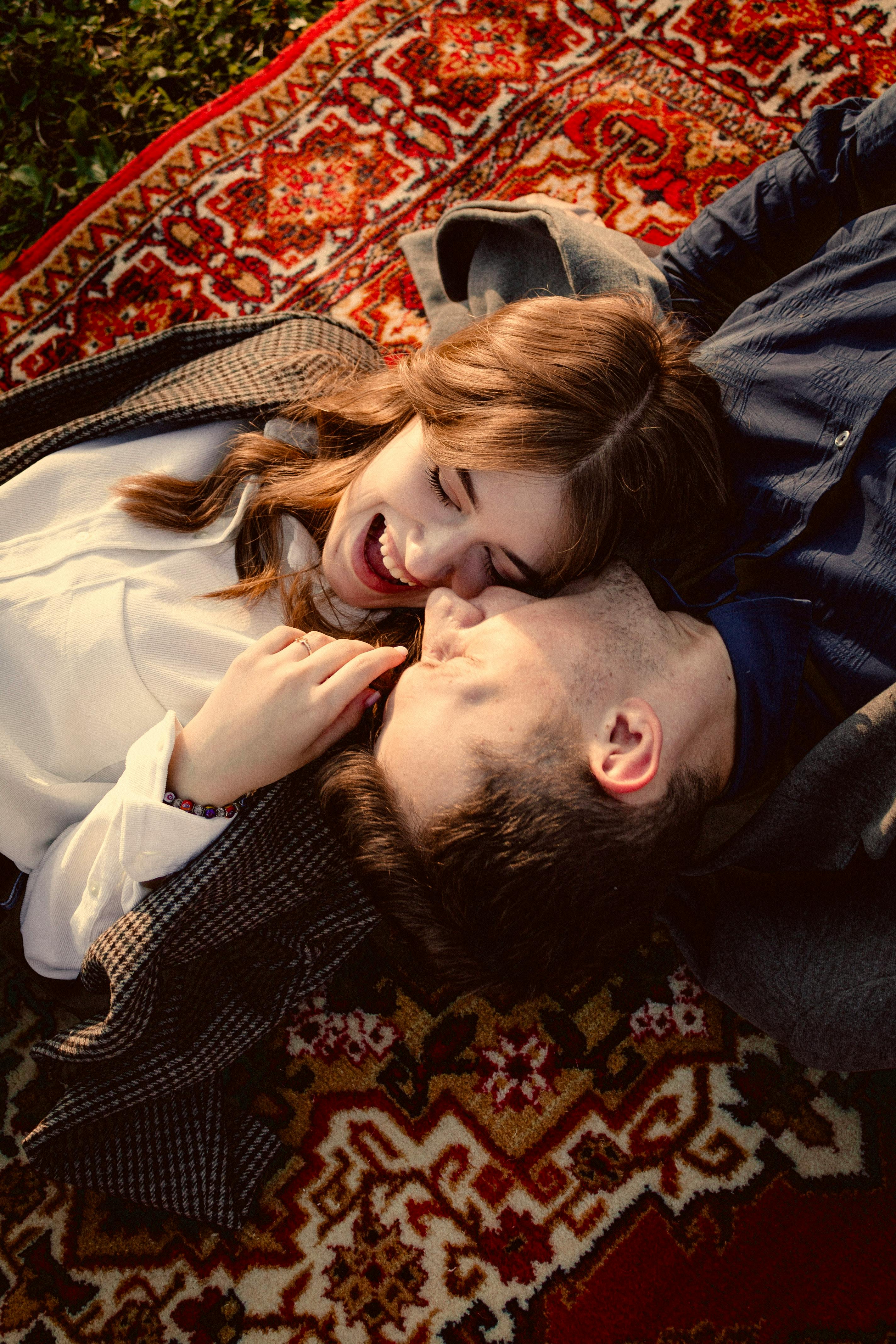 Happy couple enjoying leisure time lying on a colorful carpet outdoors, embracing and smiling.