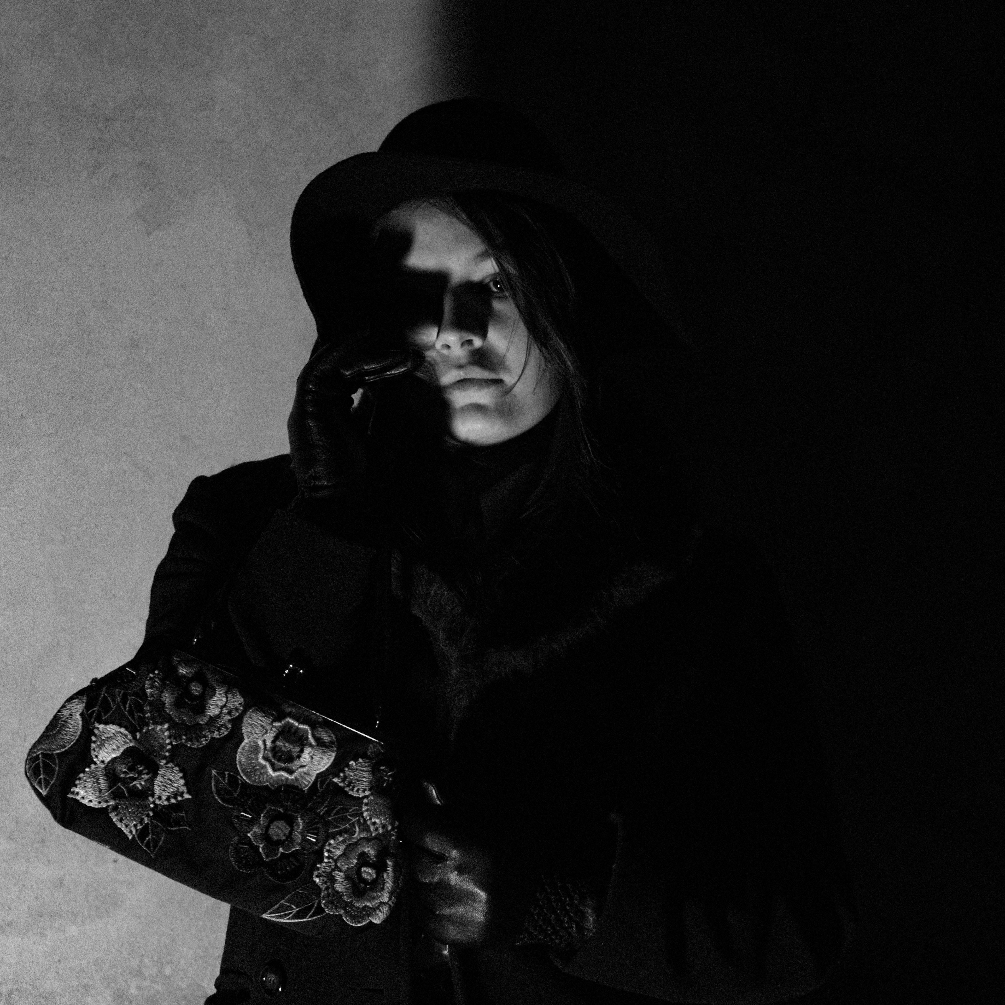Black and white portrait of a woman in shadows, holding a floral bag.