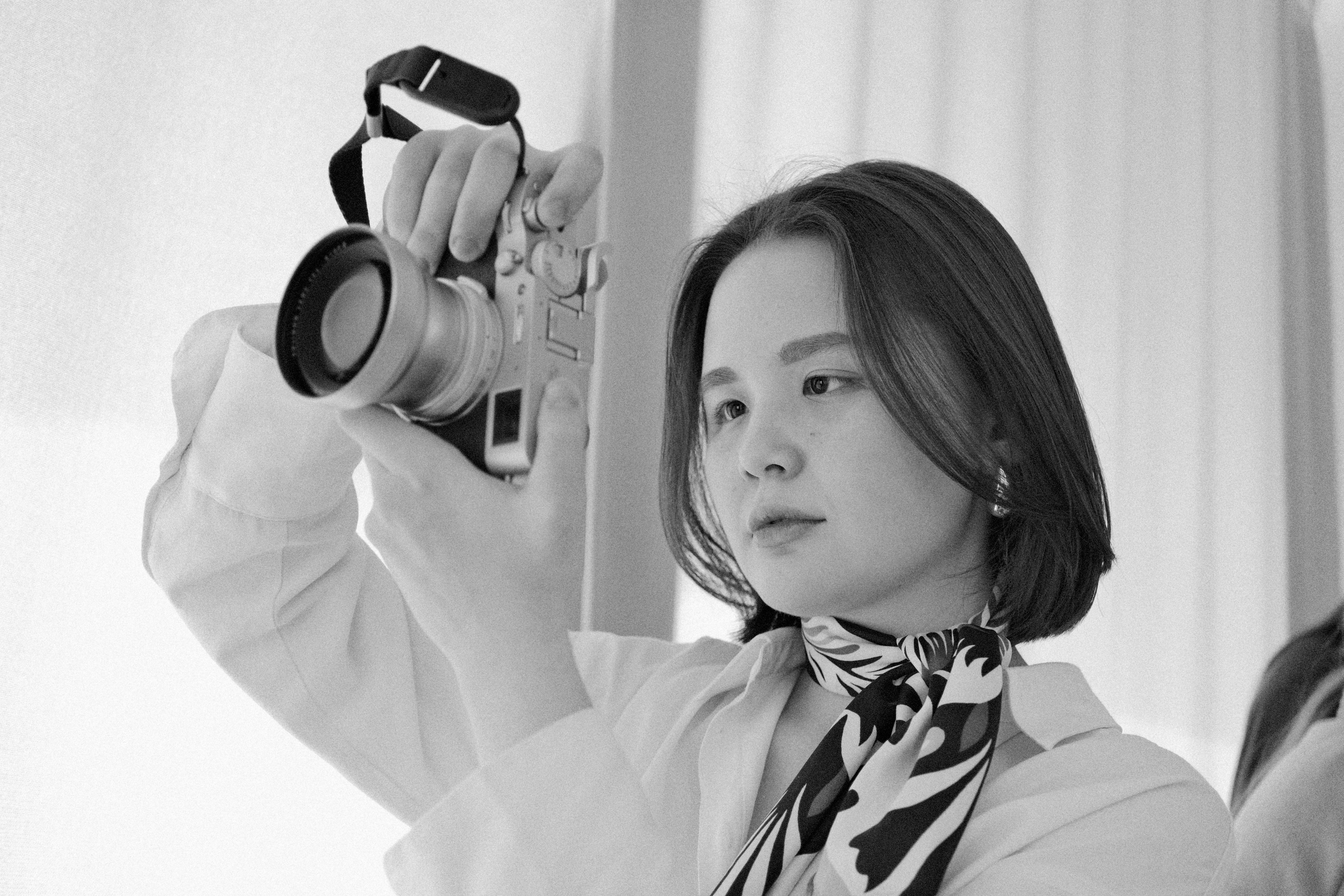 Free Artistic black and white portrait of a woman holding a vintage camera with focus and style. Stock Photo