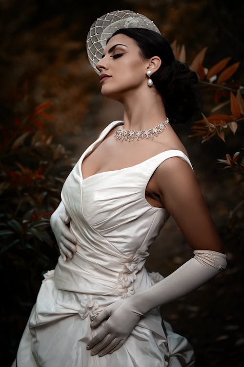 Photo of a Young Woman Posing in a White Dress, Gloves and Headdress 