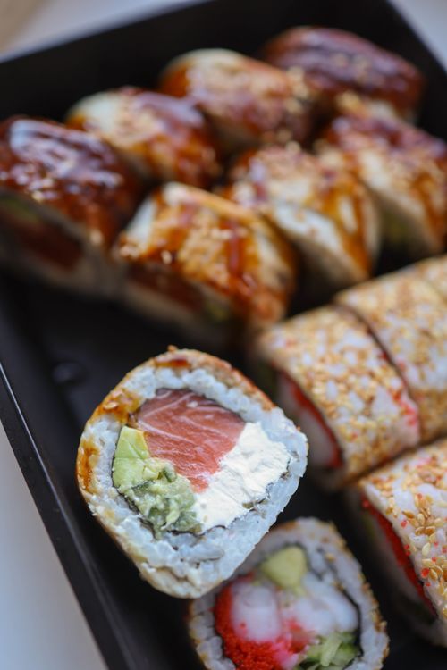 Free Close-up of assorted sushi rolls with fish, avocado, and sesame seeds in a box. Stock Photo