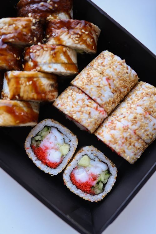 Free Delicious assorted sushi rolls with sesame seeds and fresh ingredients displayed on a black plate. Stock Photo