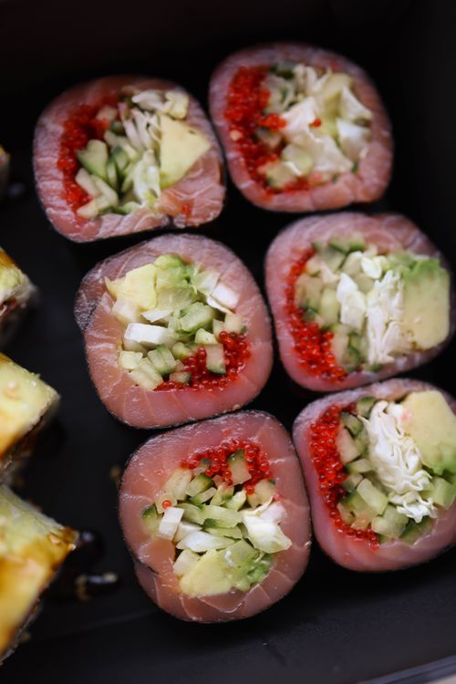 Free Colorful sushi rolls made with salmon, avocado, and cucumber on a black background. Stock Photo