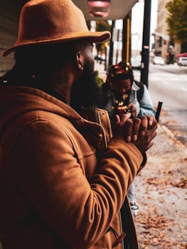 Fashion-forward man in a fedora and jacket in an urban street setting with autumn vibes.