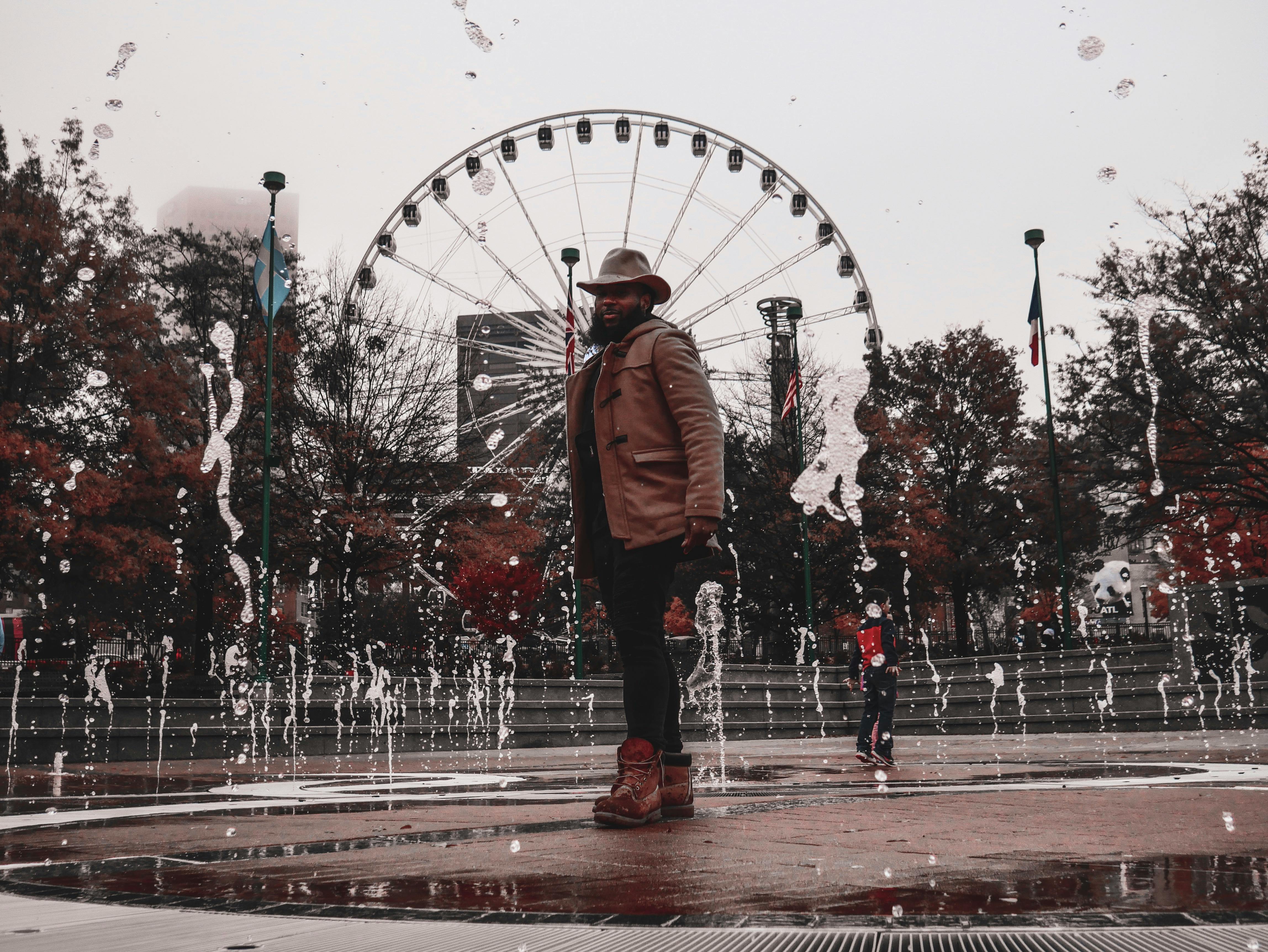 一名时尚男子带着摩天轮，在城市公园的喷泉旁摆姿势