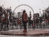 一名时尚男子带着摩天轮，在城市公园的喷泉旁摆姿势