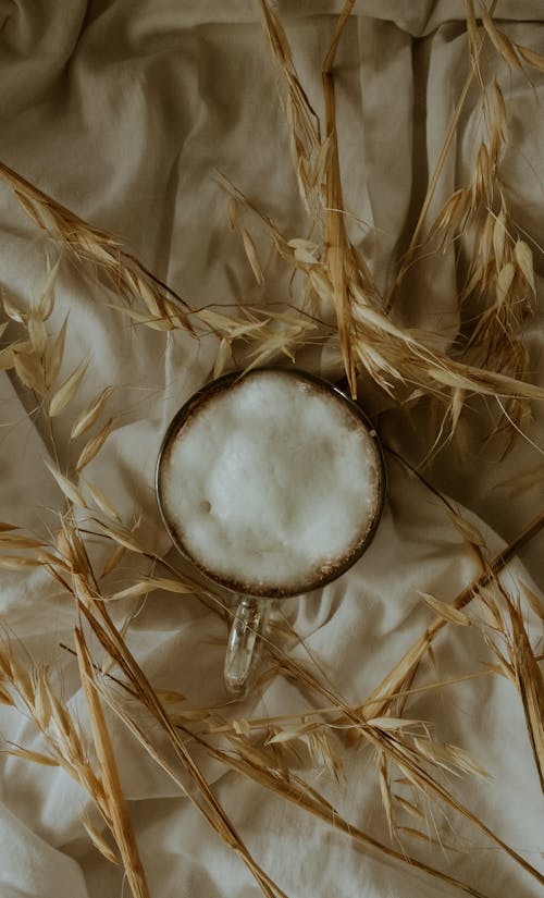A white cup of coffee on a bed of wheat