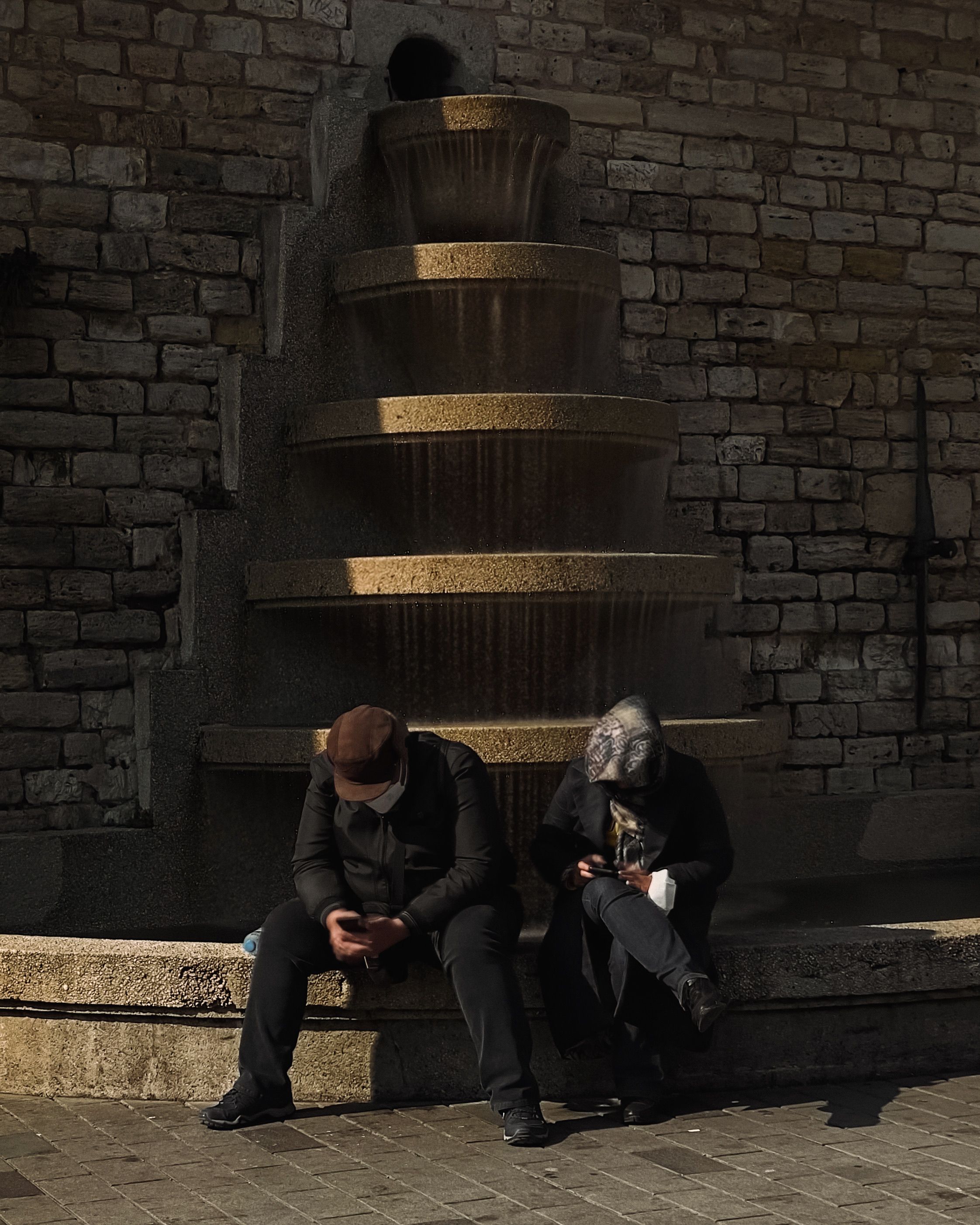 Man and Woman Sitting by Fountain in Shadow · Free Stock Photo
