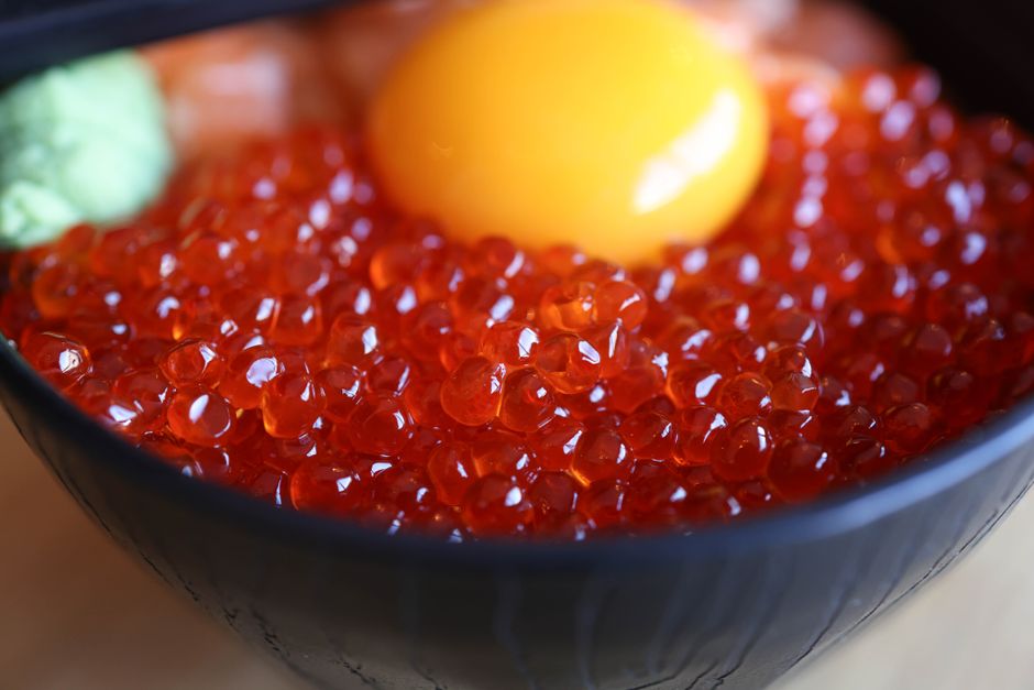 A small glass bowl of glossy orange ikura salmon roe with a mother-of-pearl spoon resting beside it