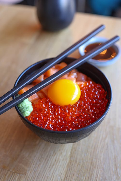 A bowl of red food with chopsticks and an egg
