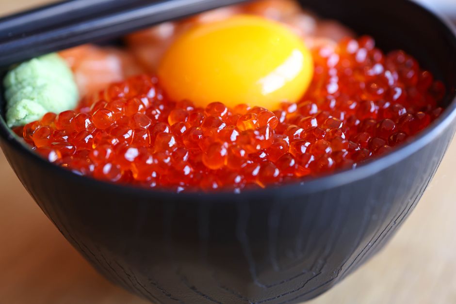 Glistening orange salmon roe pearls mounded in a small glass bowl with a mother-of-pearl spoon resting beside it
