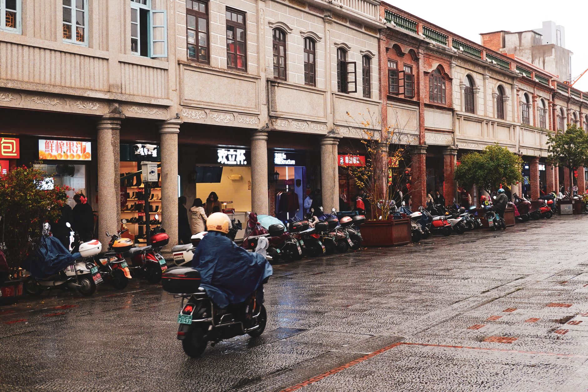 A rainy day street scene in Quanzhou, China, featuring scooters and pedestrians.