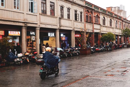 A rainy day street scene in Quanzhou, China, featuring scooters and pedestrians.