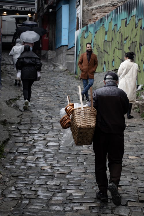 A man walking down a cobblestone street carrying a basket