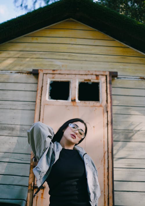 A woman in glasses and a black top is standing outside a small building