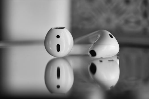 Close-up of wireless earbuds with reflection in black and white.