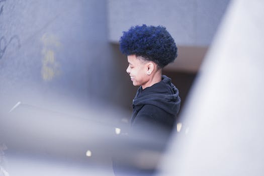 Side view of a smiling person with curly purple-blue hair standing in an urban setting.