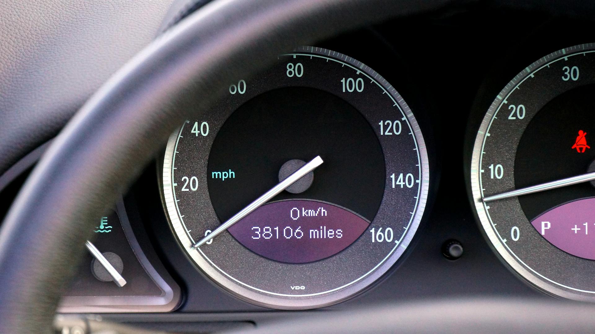 Close-up view of a car speedometer and mileage display with steering wheel in view.