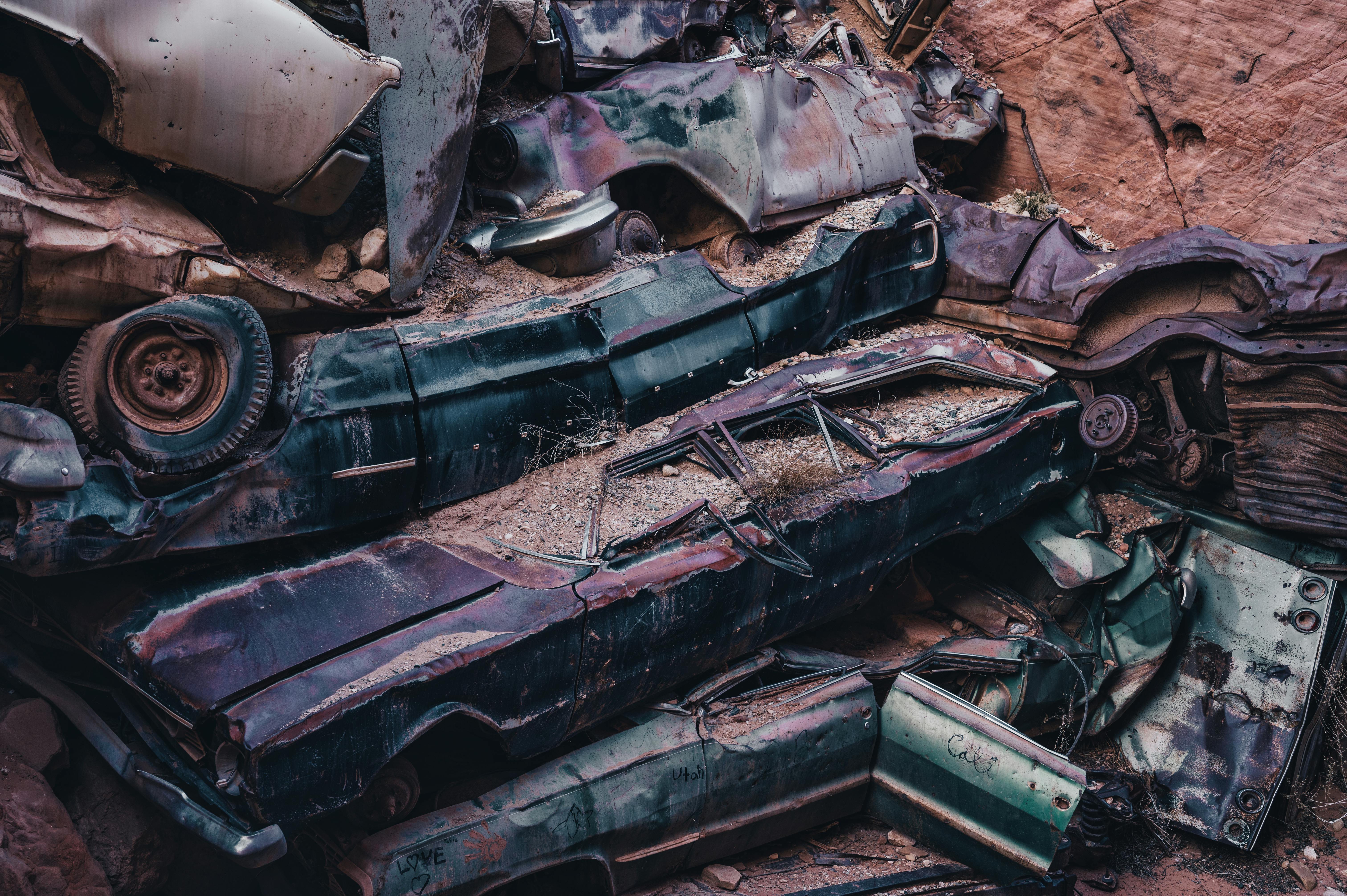 A pile of rusty, abandoned cars stacked in an outdoor junkyard.