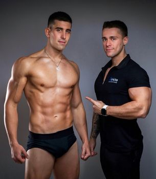 Muscular man posing with his trainer in a studio setting, showcasing fitness and strength.