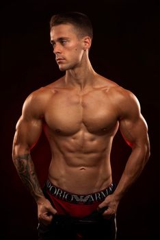 Shirtless muscular man posing in a studio setting with dramatic lighting.