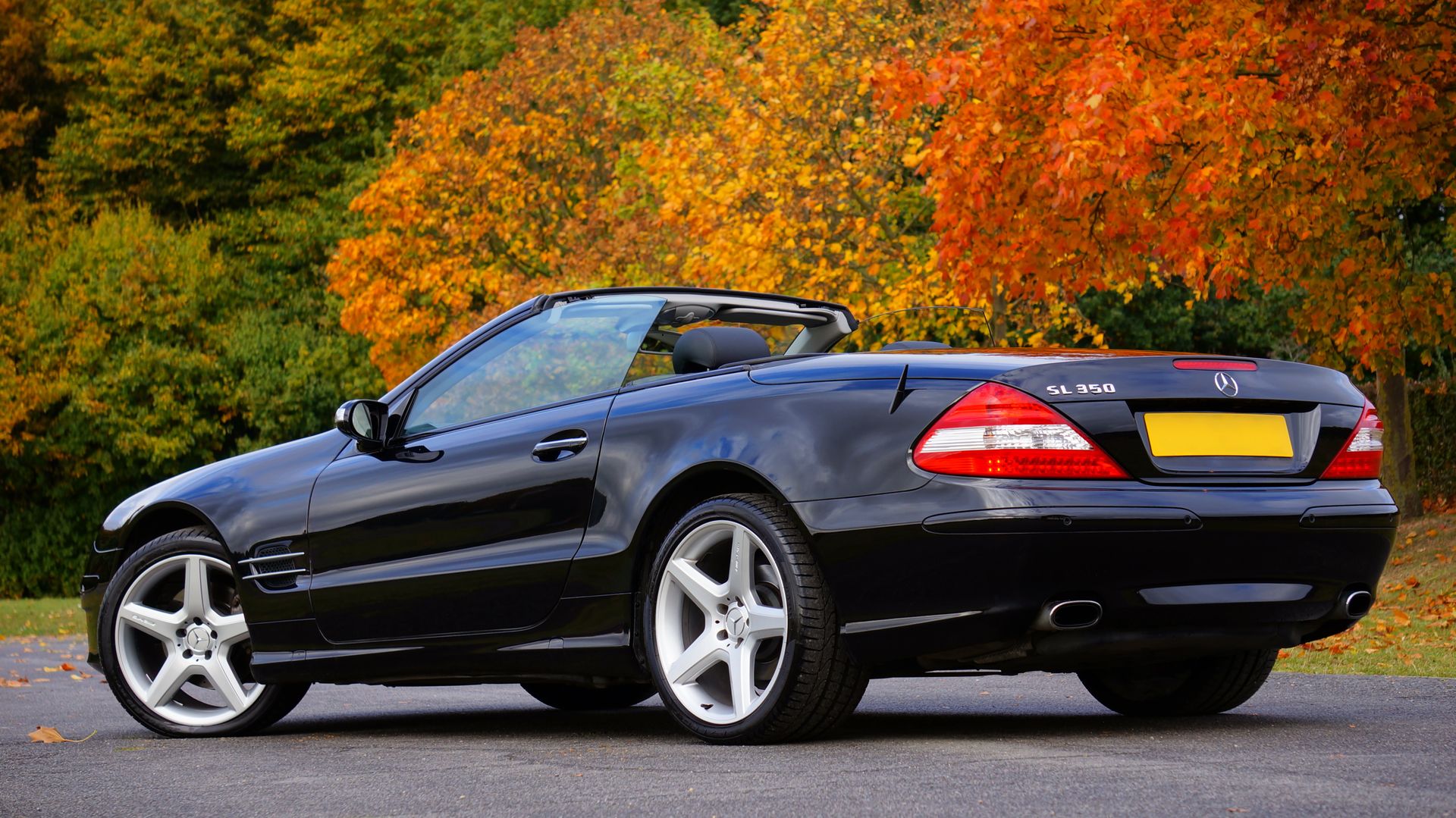 Luxury black convertible car parked outdoors with vibrant autumn foliage.
